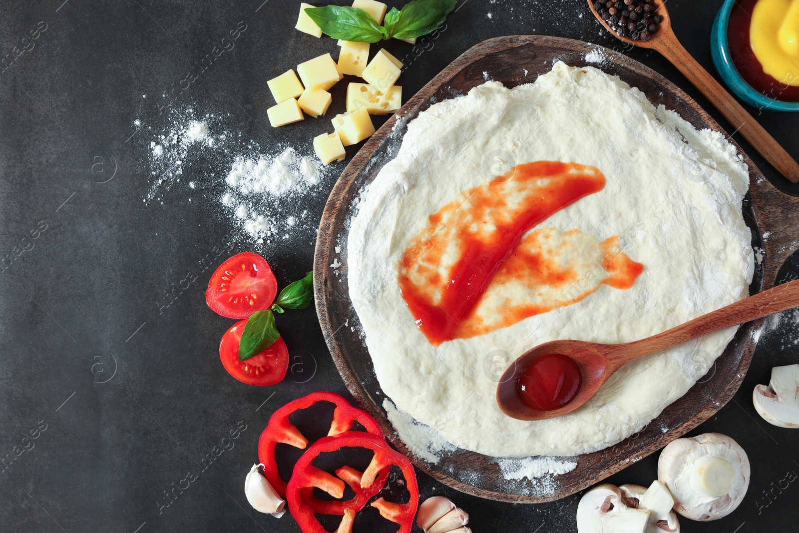 Photo of Pizza dough with tomato sauce and products on dark table, flat lay. Space for text