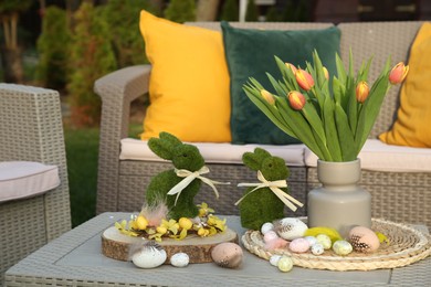 Terrace with Easter decorations. Bouquet of tulips in vase, bunny figures and decorative eggs on table outdoors