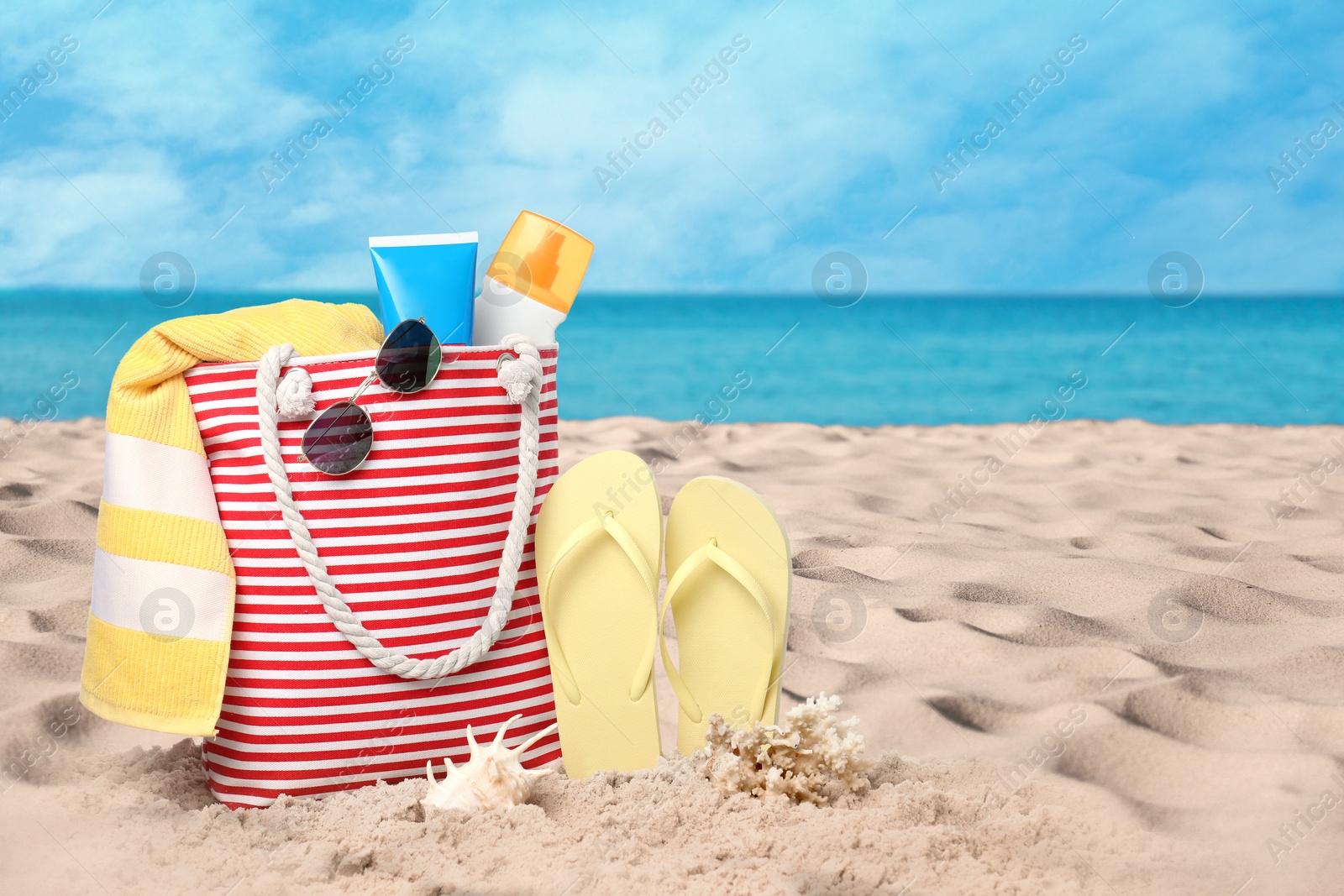 Image of Bag with accessories and cosmetics on sunny ocean beach, space for text. Summer vacation