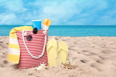 Bag with accessories and cosmetics on sunny ocean beach, space for text. Summer vacation