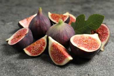 Photo of Whole and cut ripe figs with leaf on grey textured table, closeup