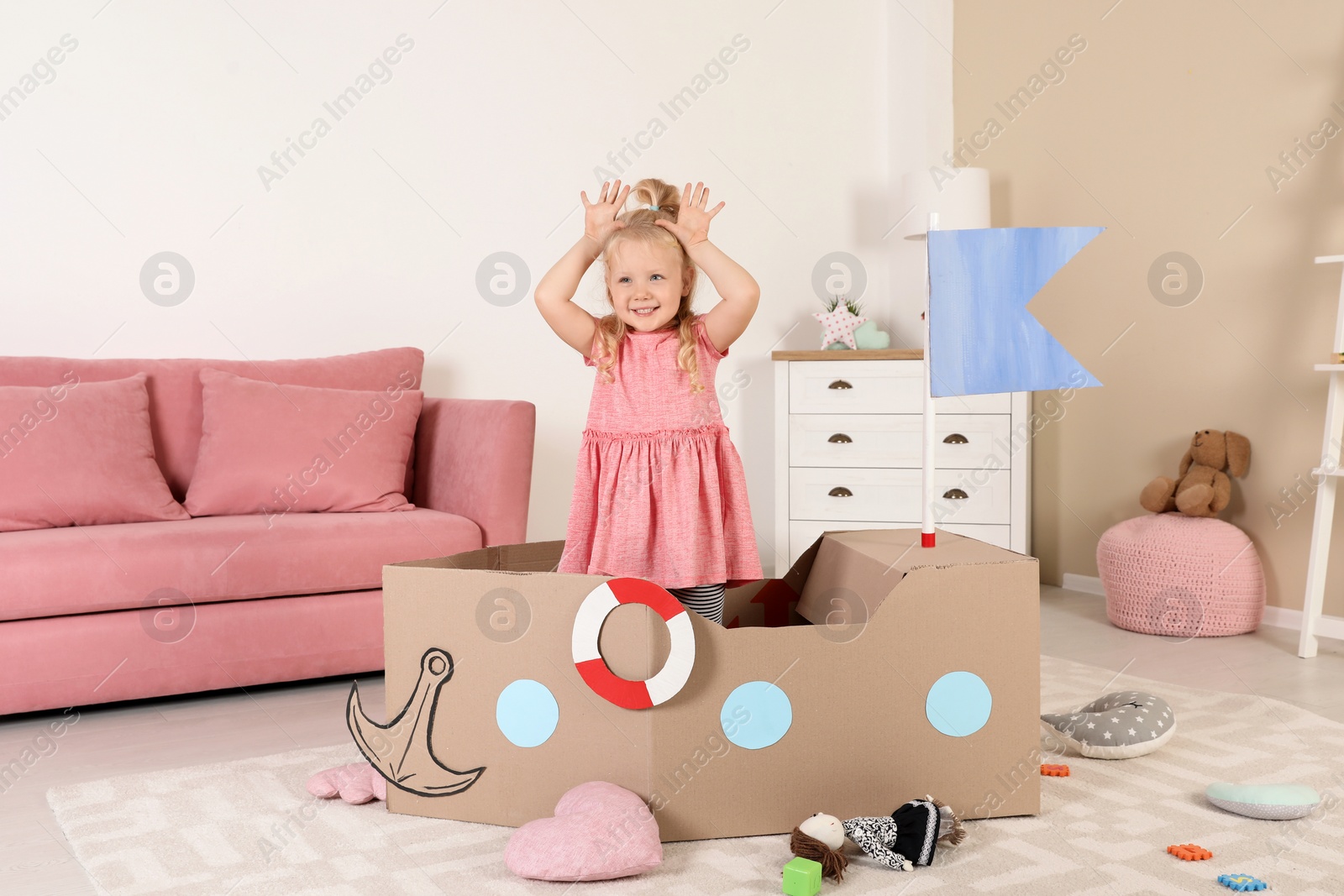 Photo of Cute little girl playing with cardboard ship at home