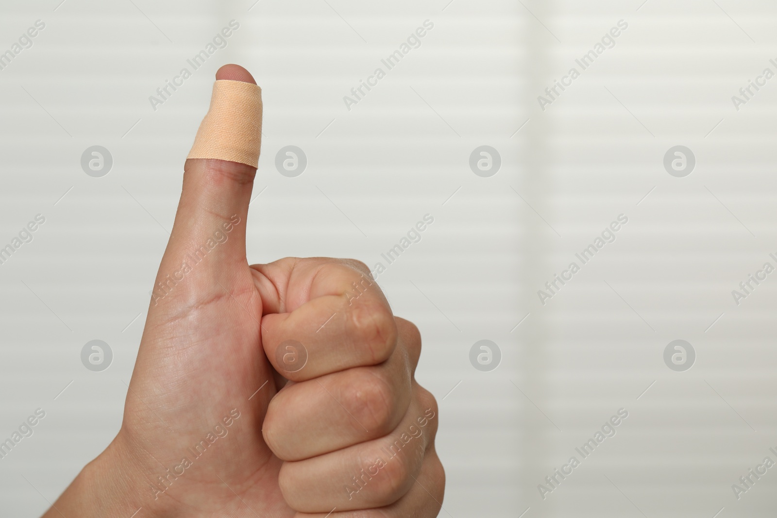 Photo of Man with sticking plaster showing thumb up indoors, closeup. Space for text