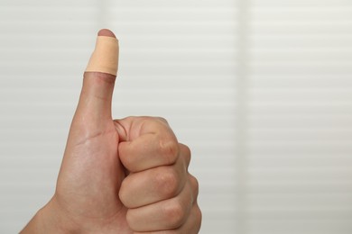 Man with sticking plaster showing thumb up indoors, closeup. Space for text