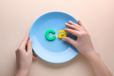 Photo of Woman and plate with calcium symbol made of colorful letters on beige background, top view