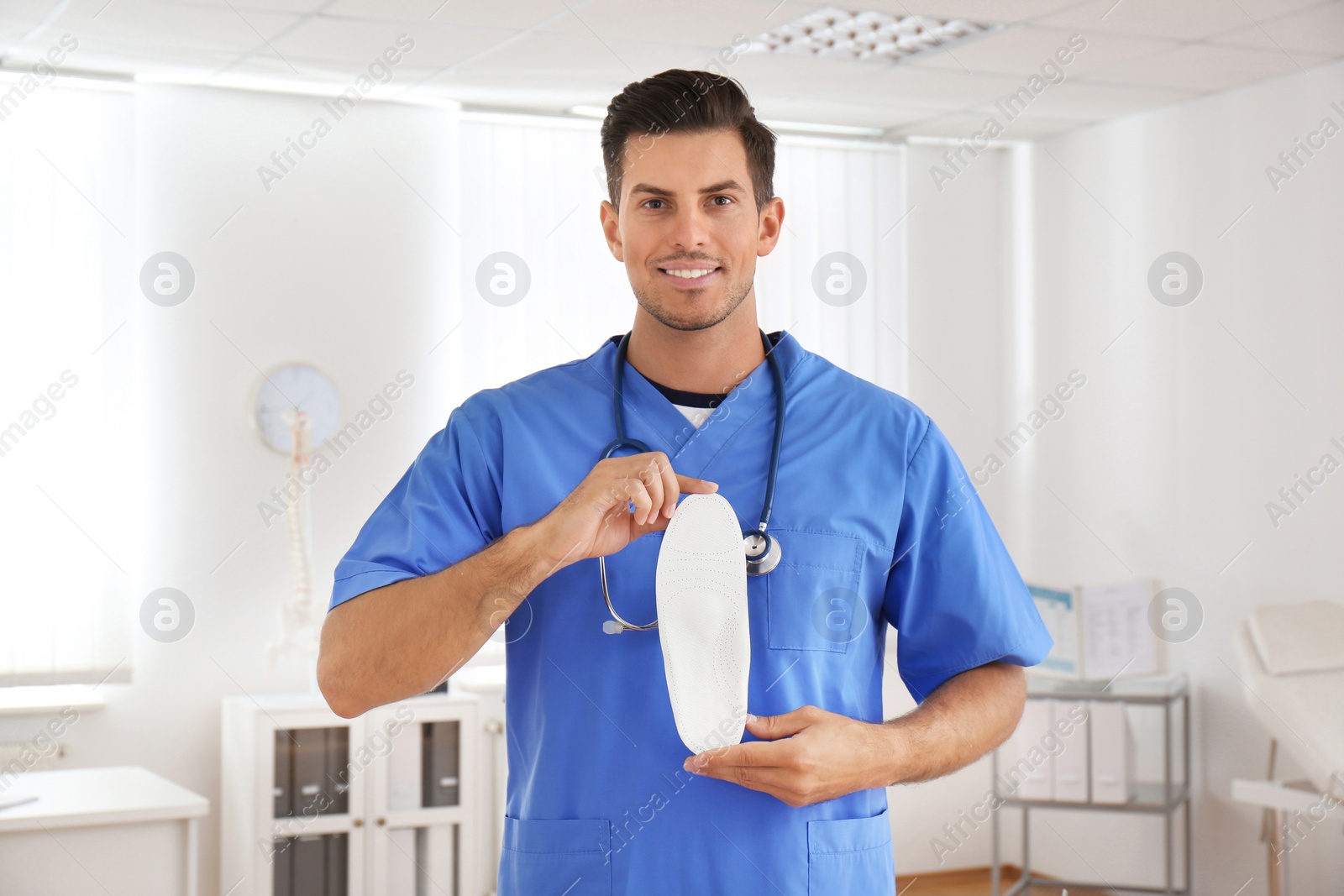 Photo of Handsome male orthopedist showing insole in clinic