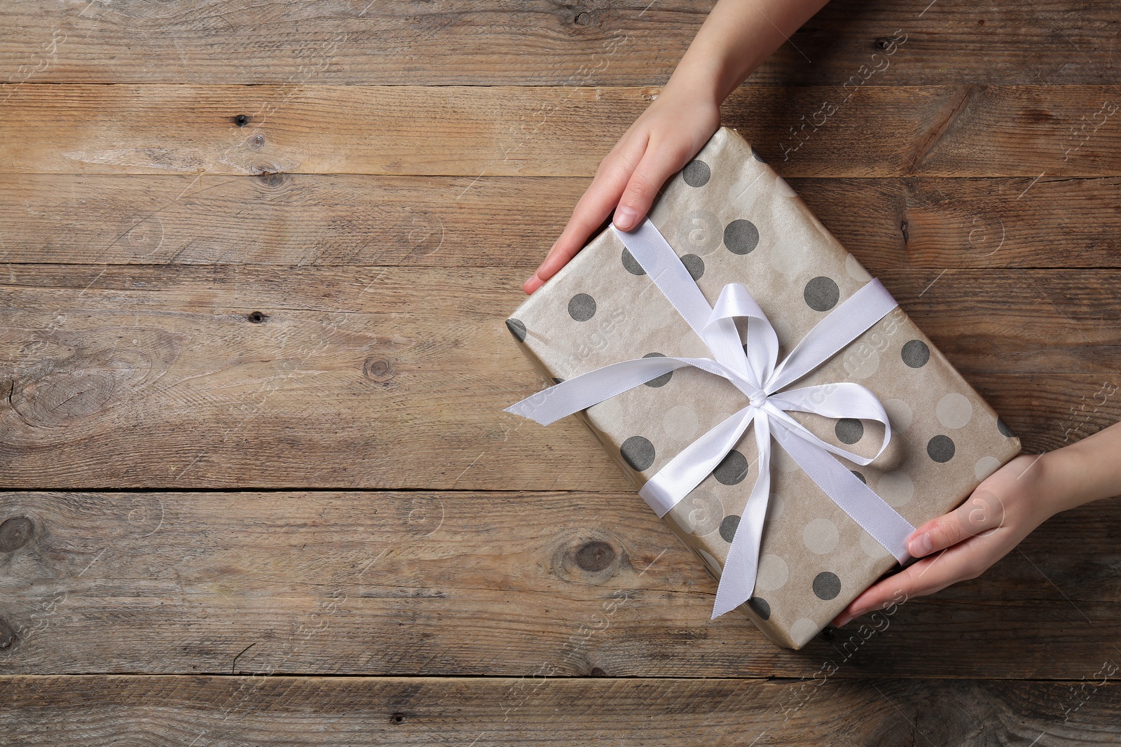 Photo of Woman holding gift box at wooden table, top view. Space for text