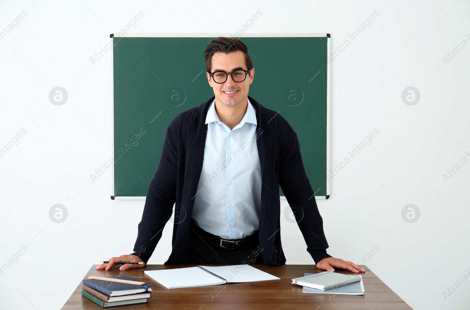 Photo of Young teacher standing near table in classroom