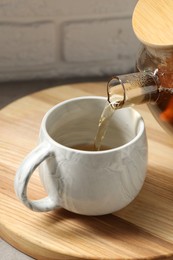 Photo of Pouring aromatic tea in cup at table, closeup