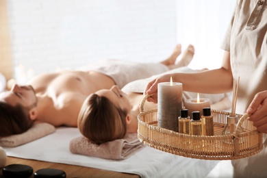 Photo of Massage therapist with spa essentials and young couple in wellness center