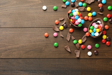 Broken chocolate egg and colorful candies on wooden table, flat lay. Space for text