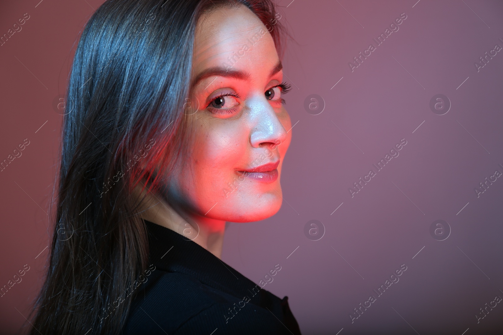Photo of Portrait of beautiful young woman on color background with neon lights. Space for text