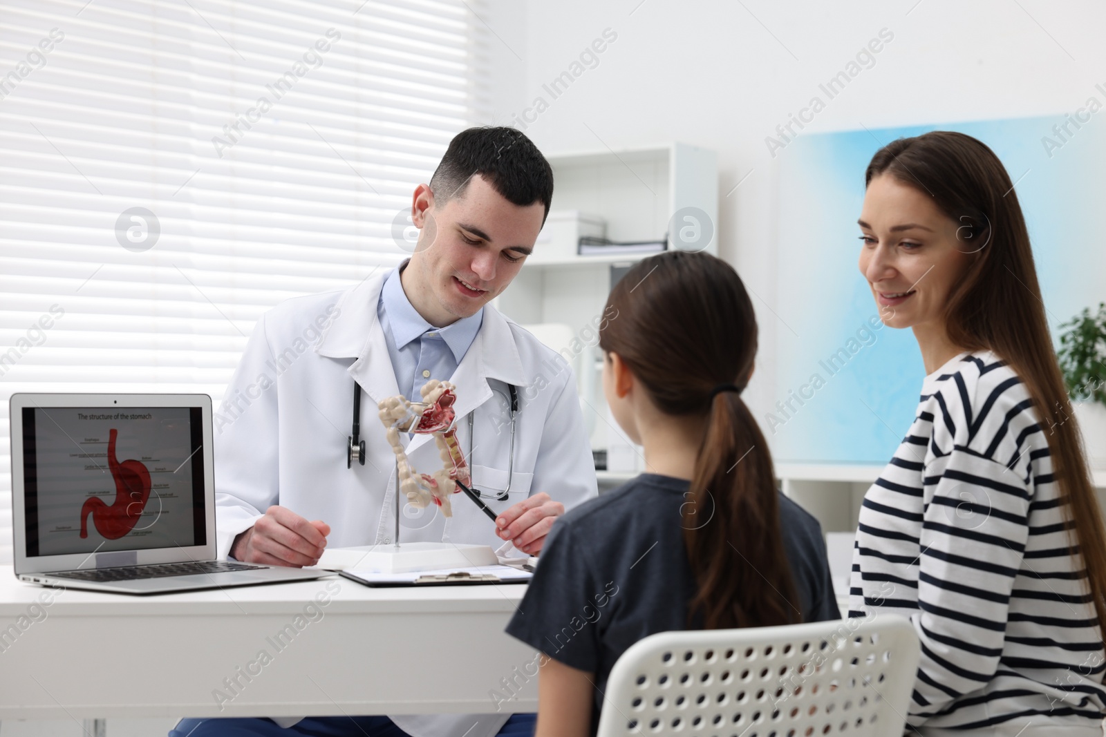 Photo of Gastroenterologist with model of intestine consulting woman and her daughter in clinic