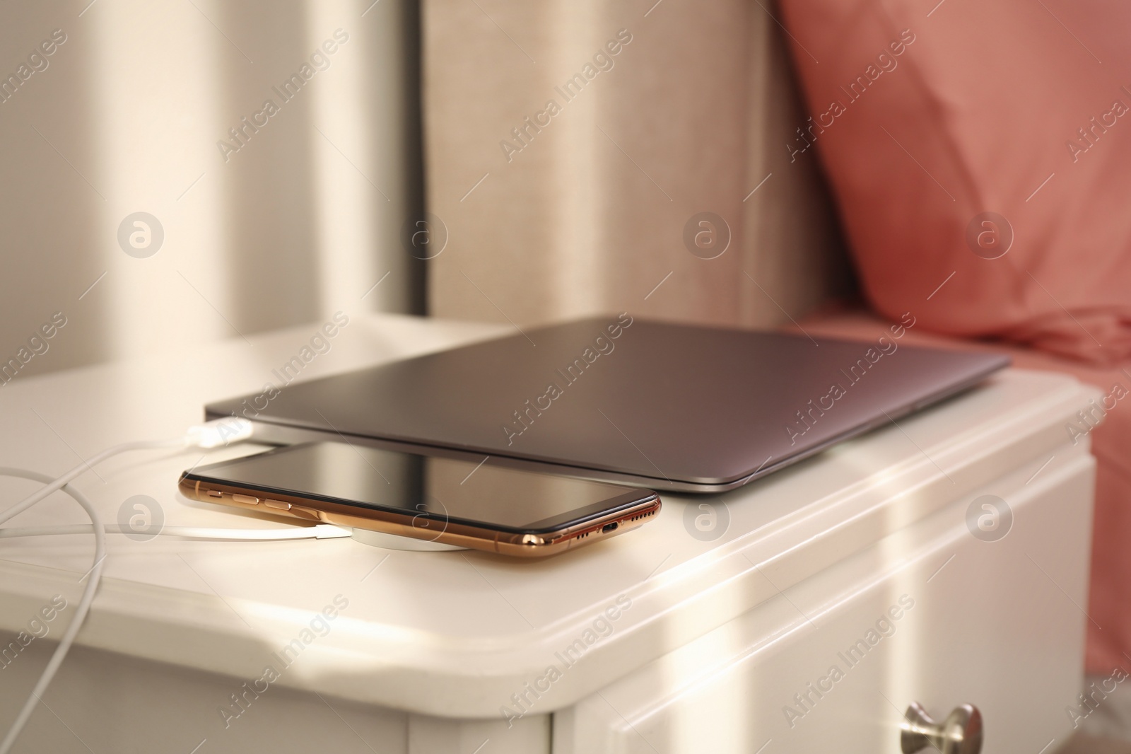 Photo of Smartphone with wireless charger connected to laptop on white table in bedroom