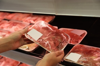 Photo of Woman choosing packed chicken meat in supermarket