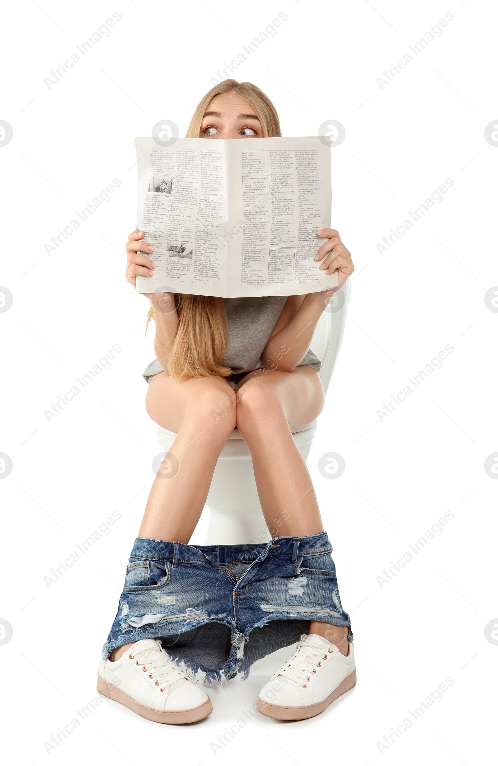 Photo of Young woman reading newspaper while sitting on toilet bowl. Isolated on white