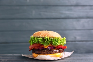 Photo of Tasty burger with bacon on table against wooden background