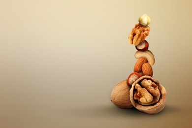 Stacked different nuts on light brown gradient background, space for text