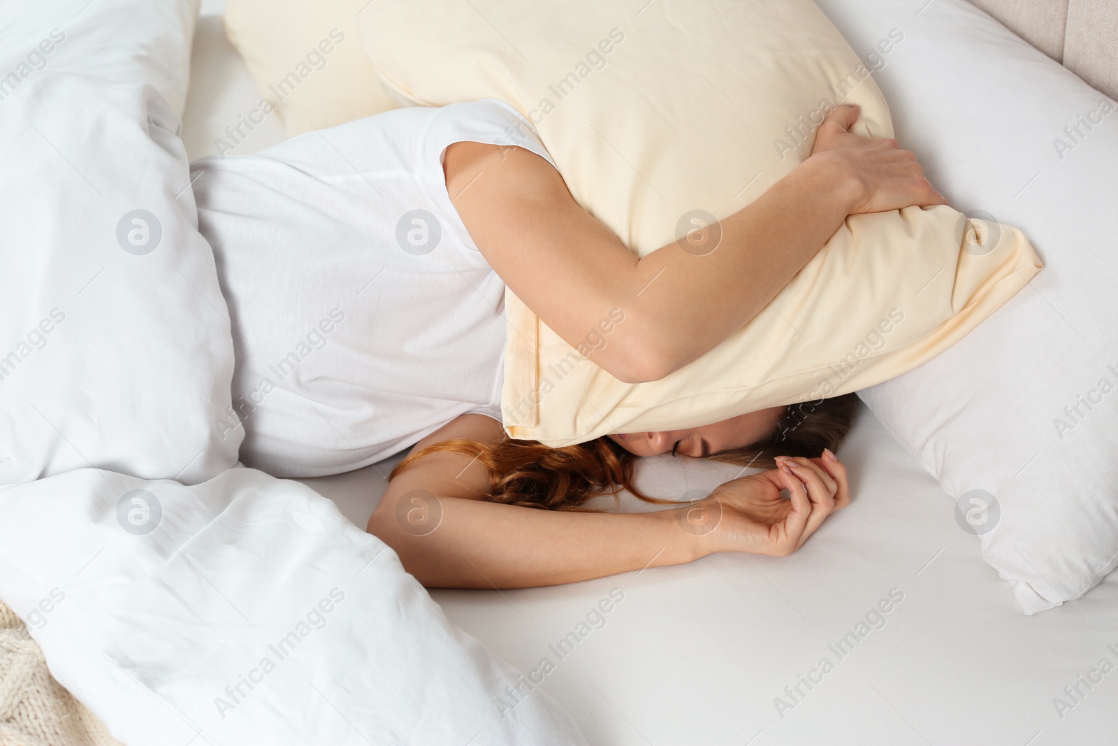 Photo of Sleepless woman covering head with pillow in bed, above view