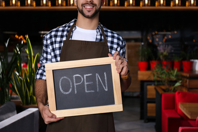 Photo of Young business owner holding sign OPEN in his cafe, closeup