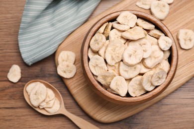 Photo of Bowl and spoon with dried banana slices on wooden table, flat lay