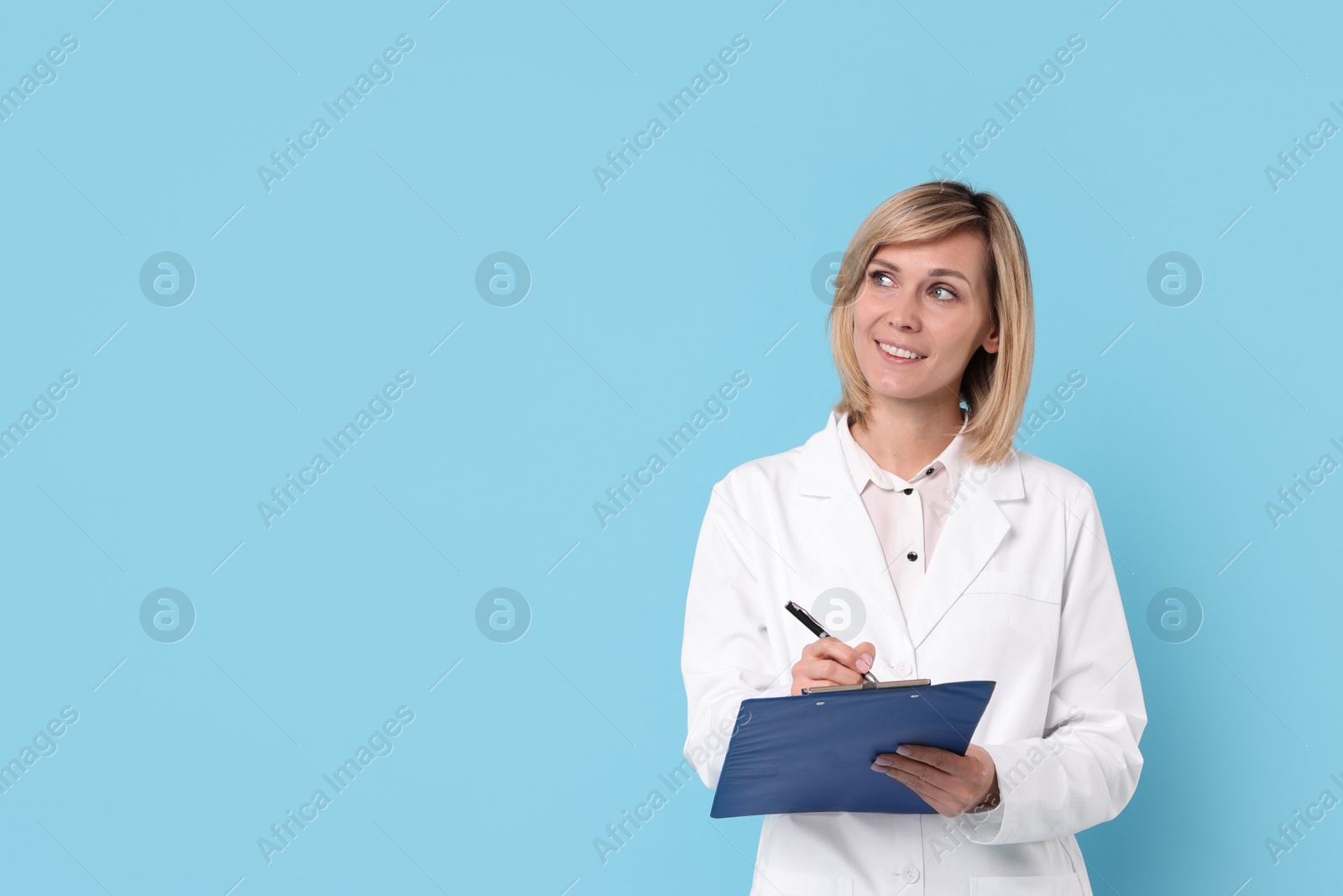 Photo of Smiling doctor with clipboard on light blue background. Space for text