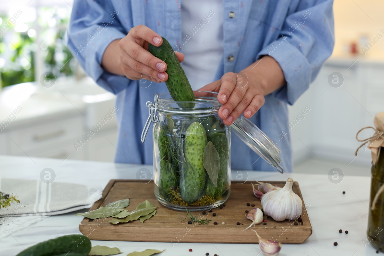 Photo of Woman putting cucumber into pickling jar at table in kitchen, closeup