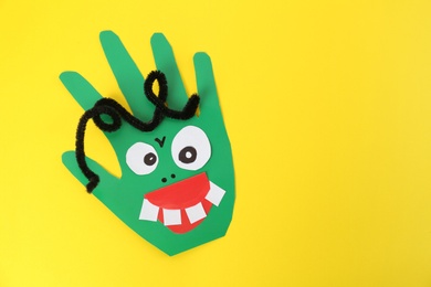 Photo of Funny green hand shaped monster on yellow background, top view with space for text. Halloween decoration