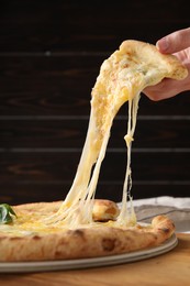 Woman taking piece of delicious cheese pizza at table, closeup