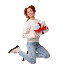 Photo of Young woman in sweater with Christmas gift jumping on white background