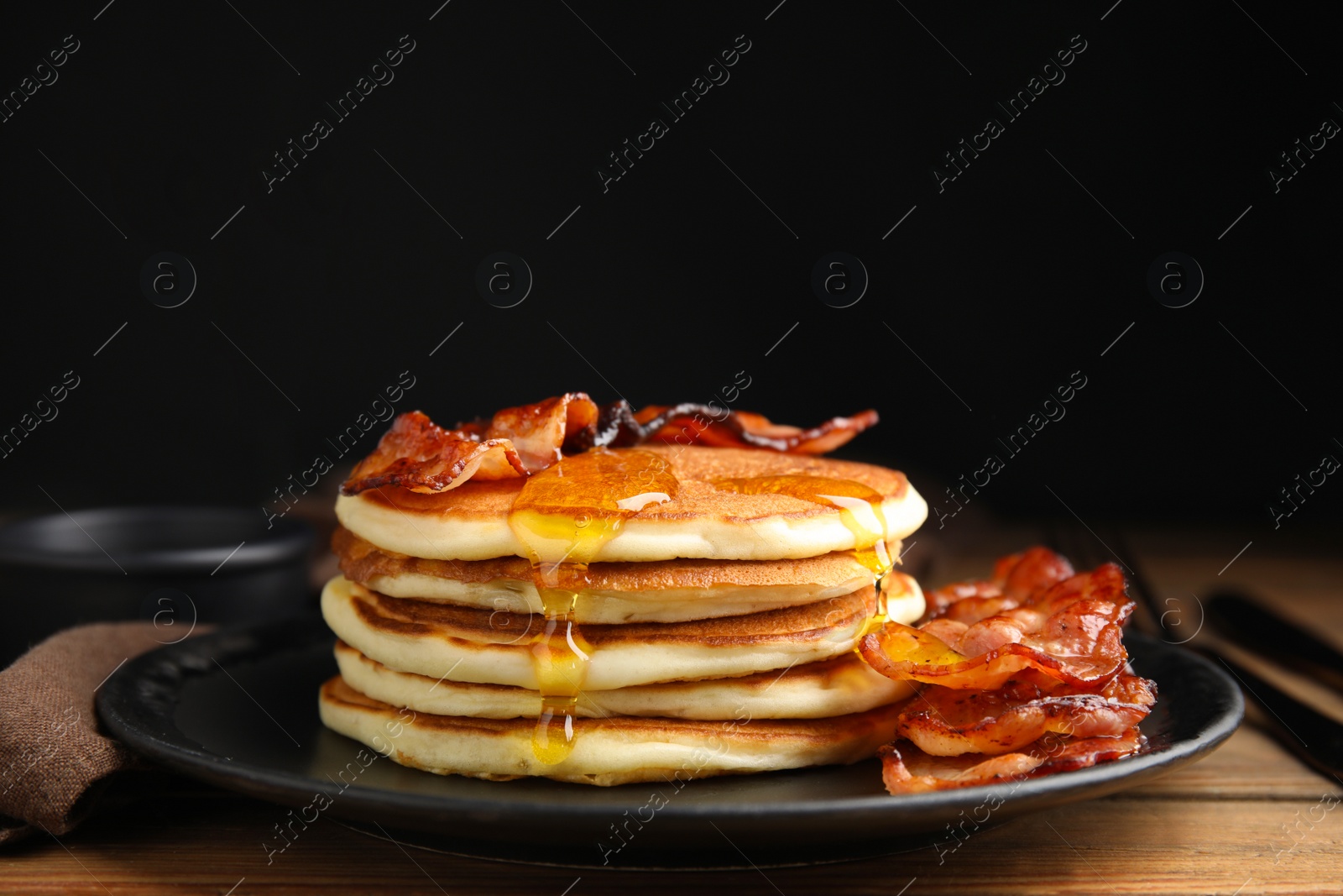 Photo of Delicious pancakes with maple syrup and fried bacon on wooden table