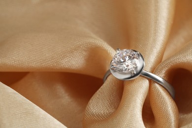Photo of Beautiful luxury engagement ring with gemstone on beige fabric, closeup