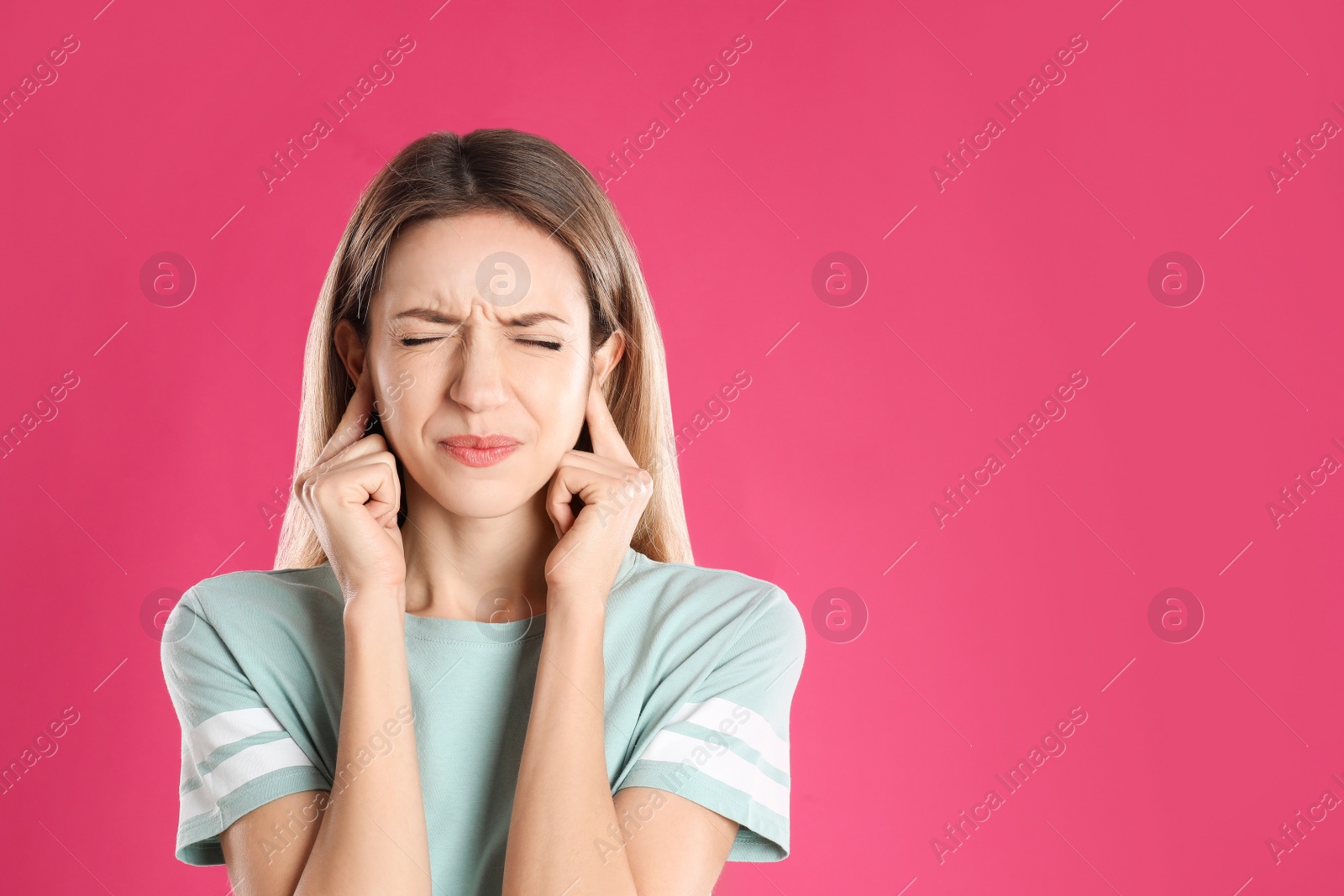 Photo of Emotional young woman covering her ears with fingers on pink background. Space for text