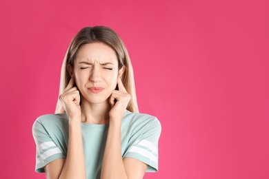 Emotional young woman covering her ears with fingers on pink background. Space for text