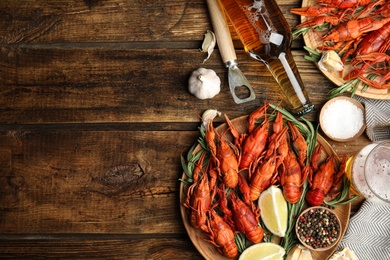 Flat lay composition with delicious red boiled crayfishes on wooden table, space for text