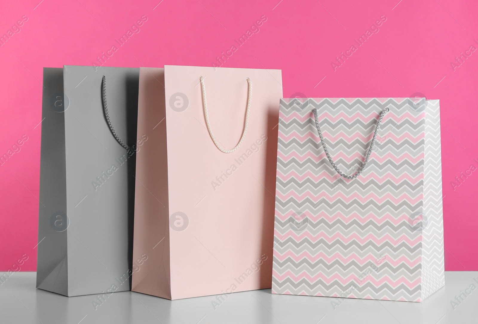 Photo of Gift bags on white table against pink background