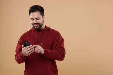 Happy young man using smartphone on beige background, space for text