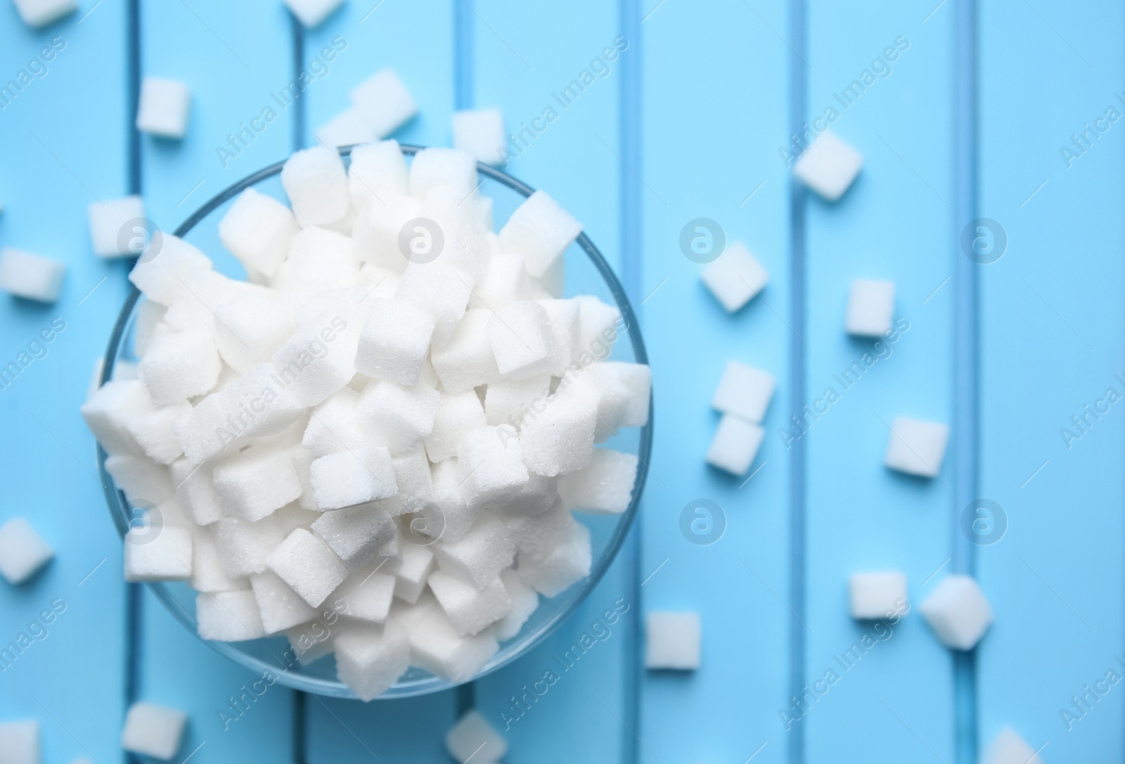 Photo of Bowl with refined sugar cubes on color wooden background, top view