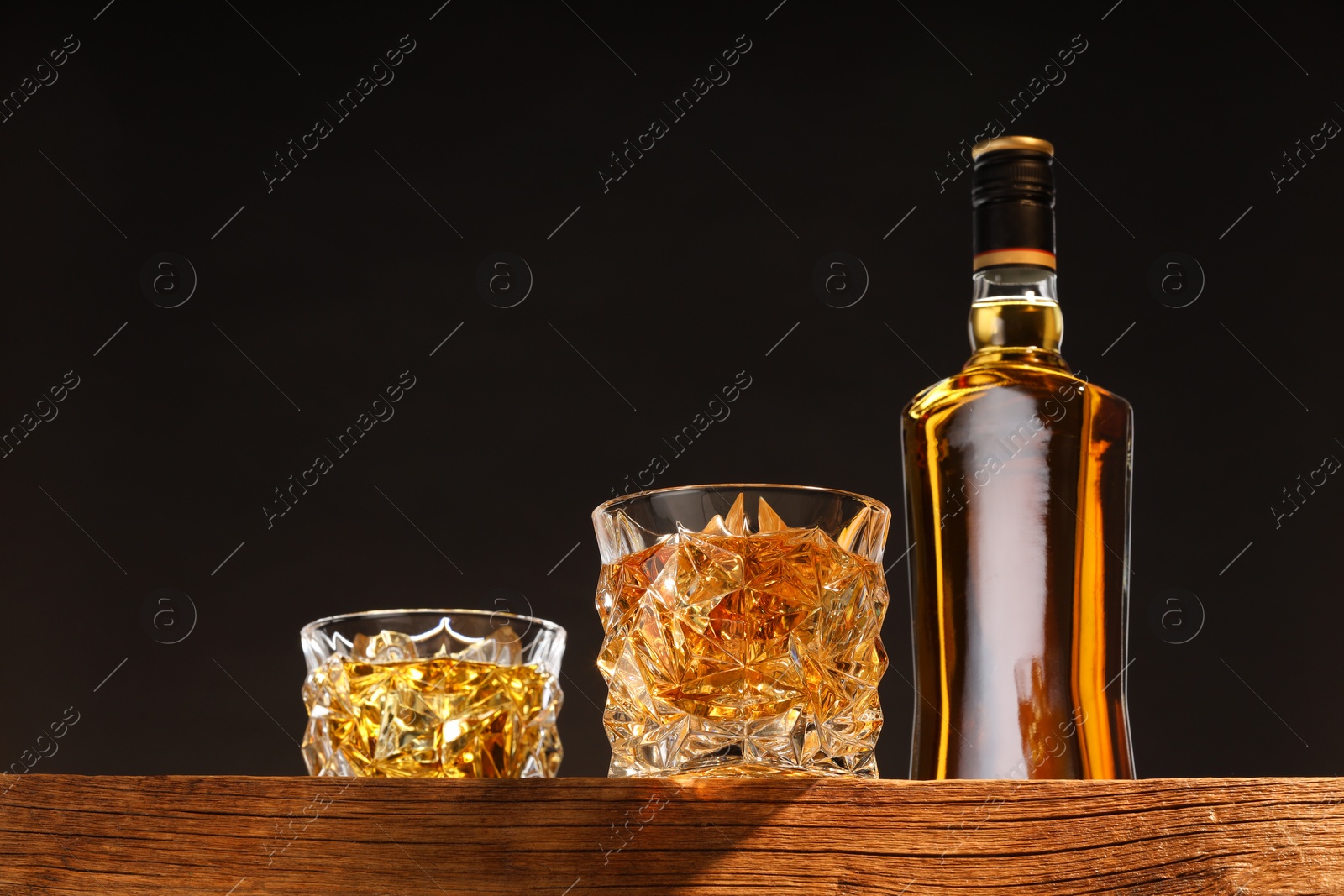 Photo of Whiskey in glasses and bottle on wooden table, low angle view