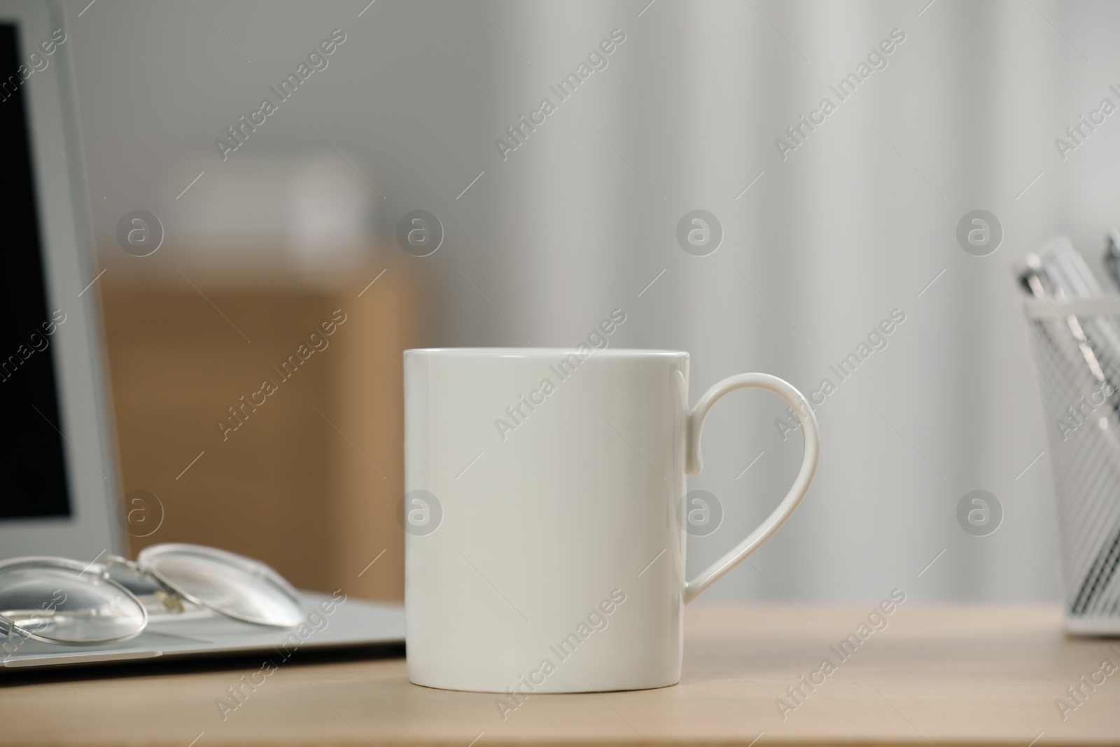 Photo of White ceramic mug, glasses and laptop on wooden table at workplace