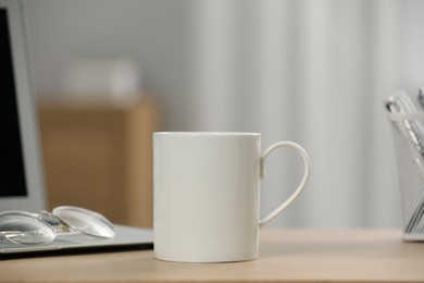 White ceramic mug, glasses and laptop on wooden table at workplace