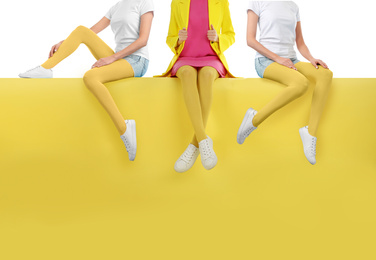 Women wearing yellow tights and stylish shoes sitting on color background, closeup 