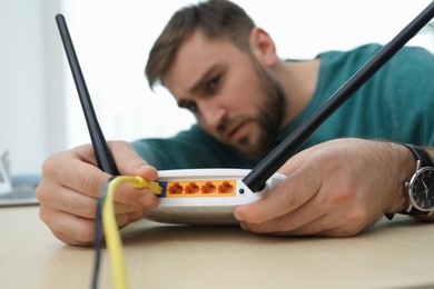 Photo of Man connecting cable to router at wooden table, focus on hand. Wireless internet communication