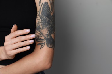 Photo of Woman applying cream on her arm with tattoos against light grey background, closeup