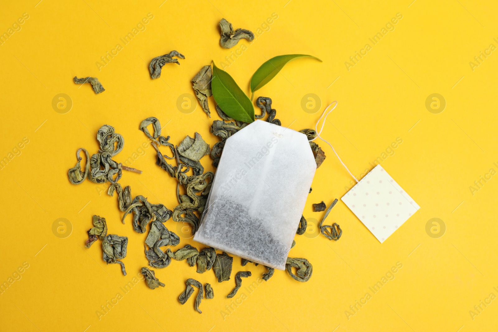 Photo of Tea bag with scattered dry leaves on color background, top view