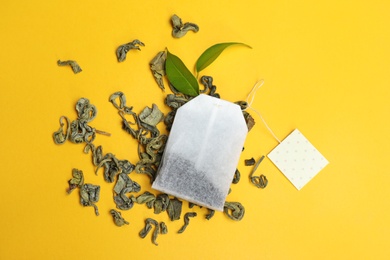 Tea bag with scattered dry leaves on color background, top view