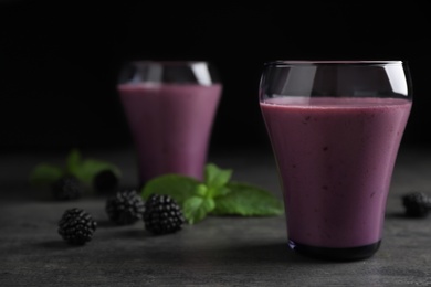 Photo of Glasses with blackberry yogurt smoothies on grey table against dark background