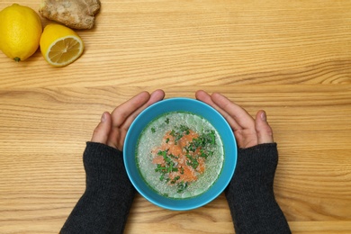 Photo of Man with bowl of soup at wooden table, top view. Flu treatment