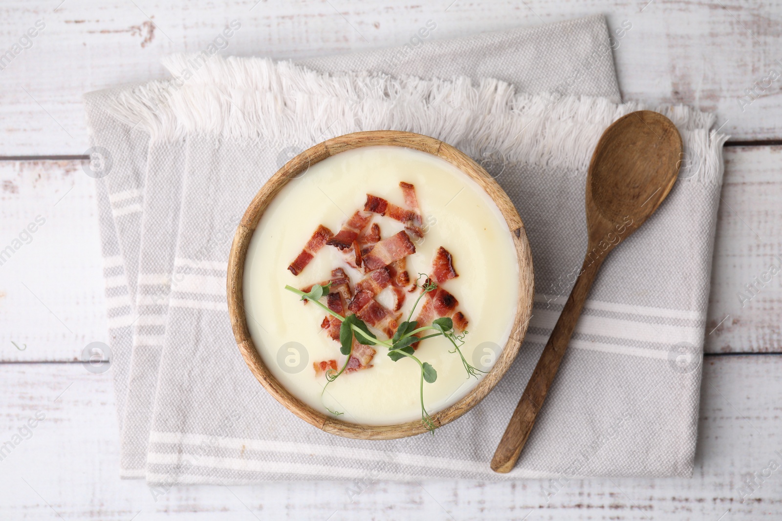 Photo of Delicious potato soup with bacon and microgreens in bowl served on wooden table, flat lay