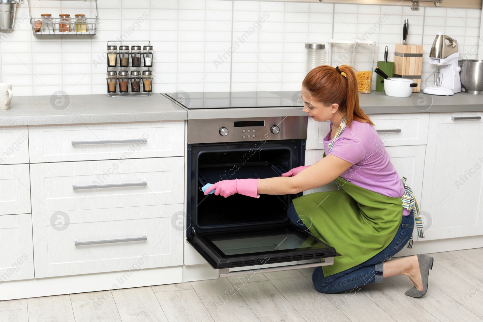 Photo of Woman cleaning oven tray with rag in kitchen